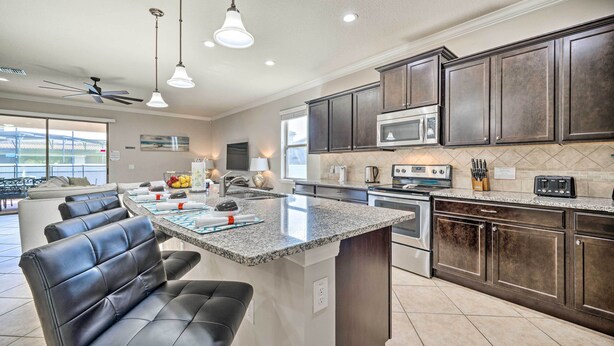 A modern kitchen with dark wood cabinets, a granite countertop, and a central island with seating. - Kissimmee Retreat With Private Pool & Spa (Kissimmee)