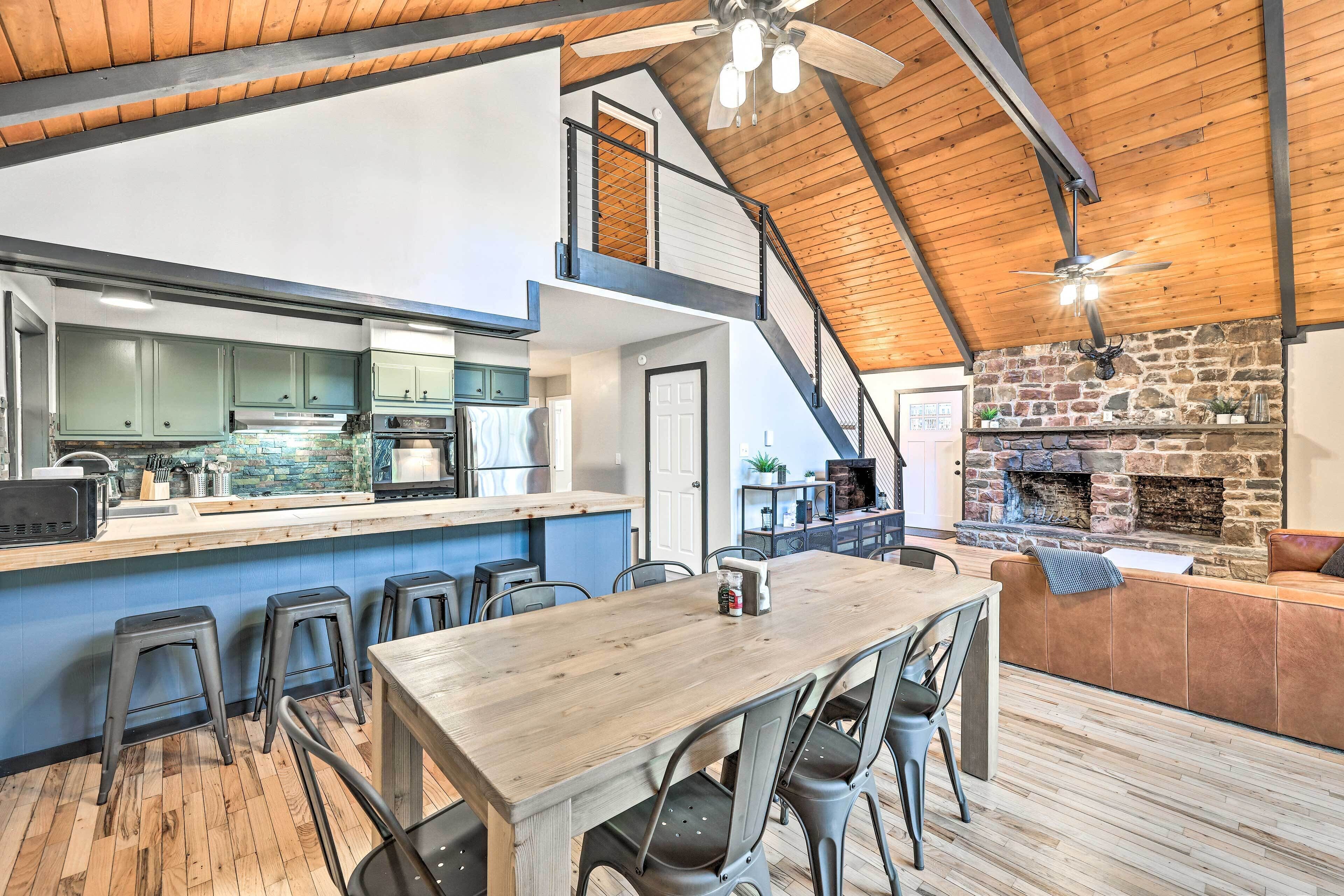 A spacious kitchen with a wooden ceiling, a stone fireplace, and a dining area with stools.