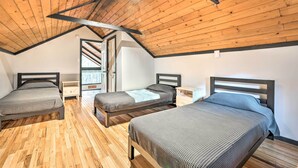 A bedroom with two beds, wooden flooring, and a sloped ceiling. - Game Room, Fire Pit & Deck: Spacious Poconos Home! (Lake Harmony)