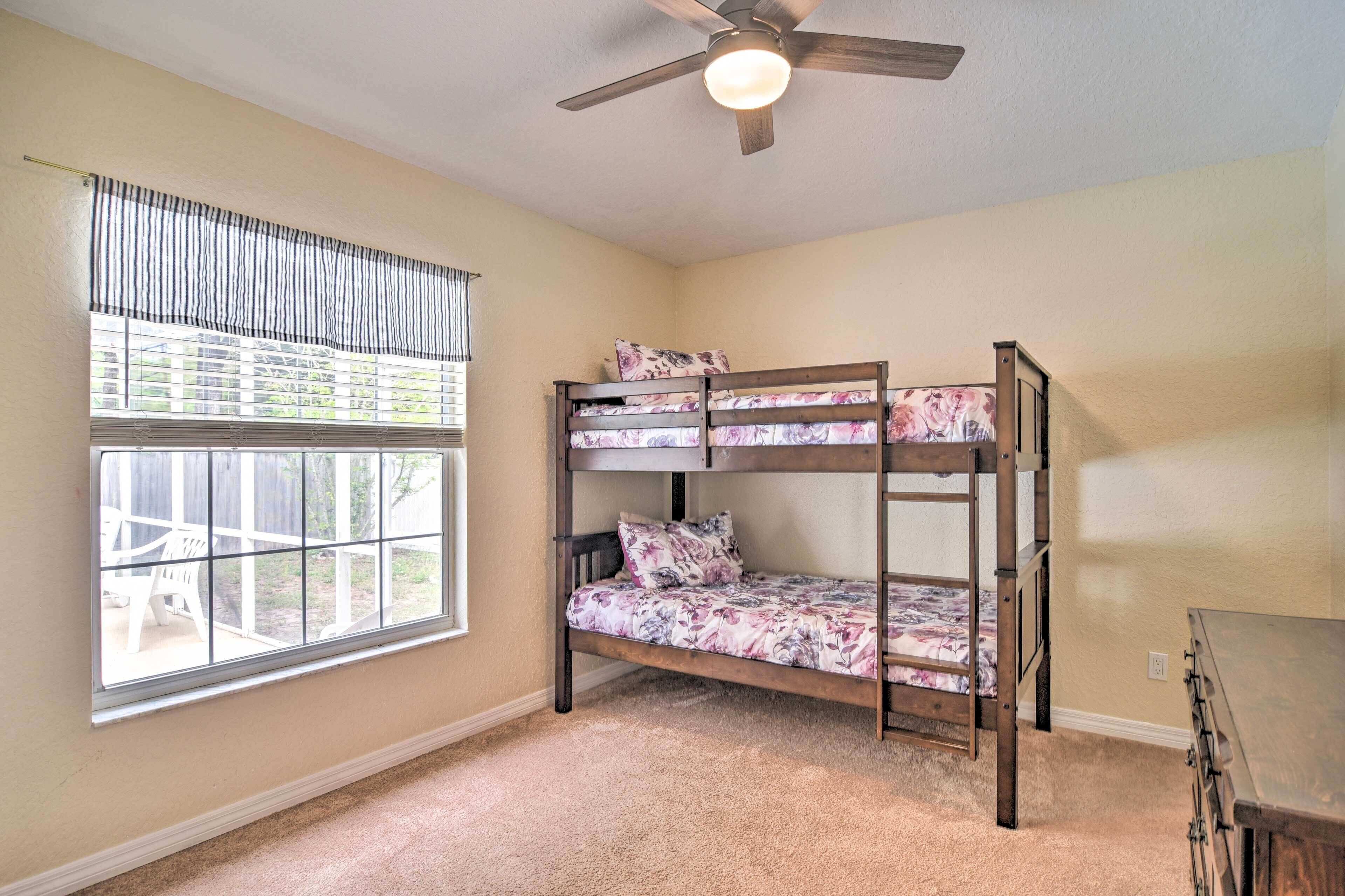 A room with bunk beds, a ceiling fan, a window with blinds, and a carpeted floor.