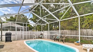 A covered swimming pool with a grill and chairs, surrounded by a wooden fence and trees. - Coastal Getaway w/ Pool: 6 Mi to St Pete Beach! (St. Petersburg)