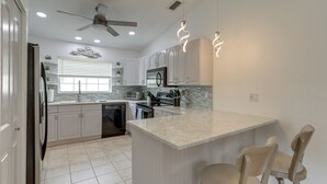 A modern kitchen with white cabinetry, a central island, and bar stools. - Coastal Getaway w/ Pool: 6 Mi to St Pete Beach! (St. Petersburg)
