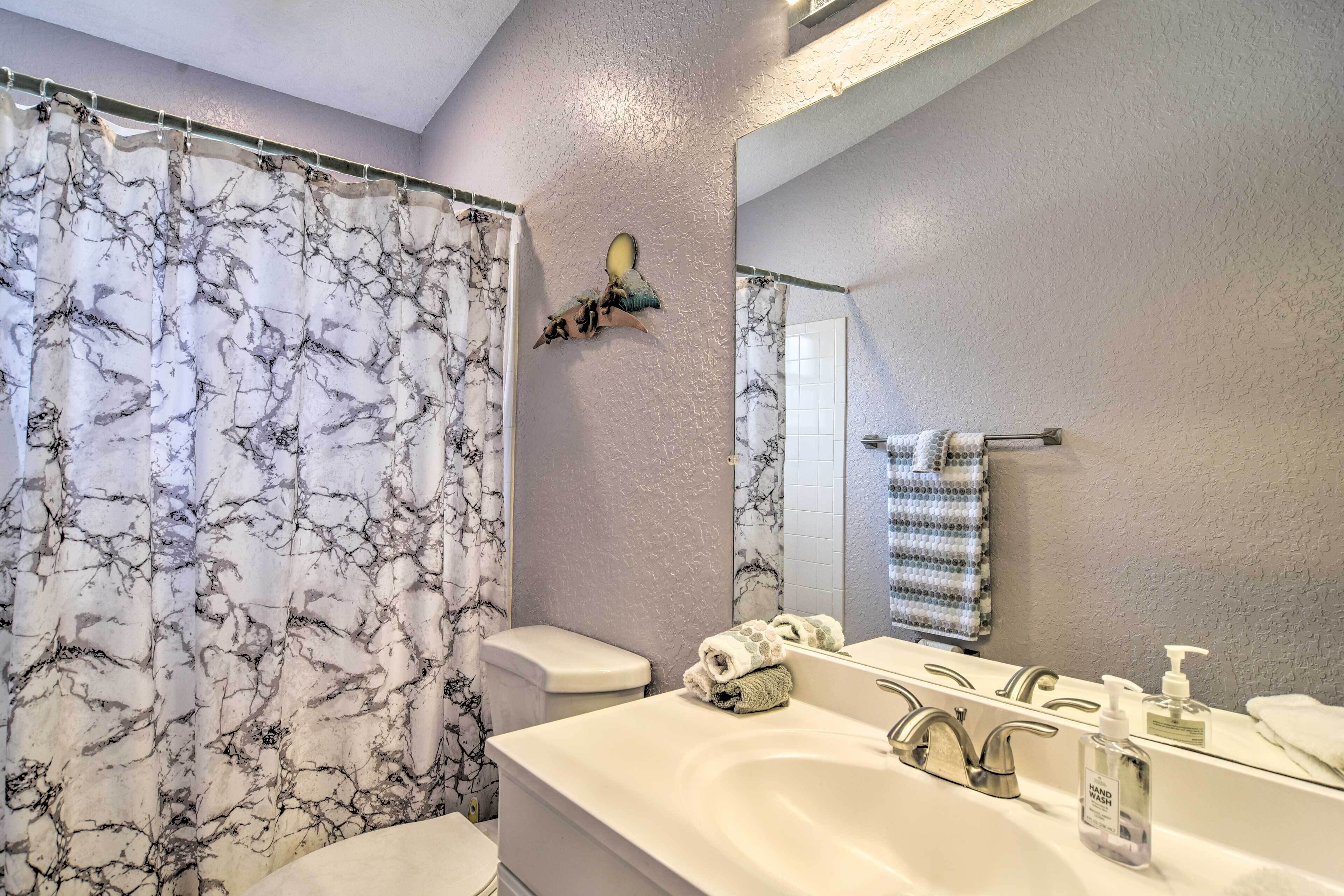 Een badkamer met een douchegordijn met marmerprint, een toilet, een wastafel met spiegel en een handdoekhouder.