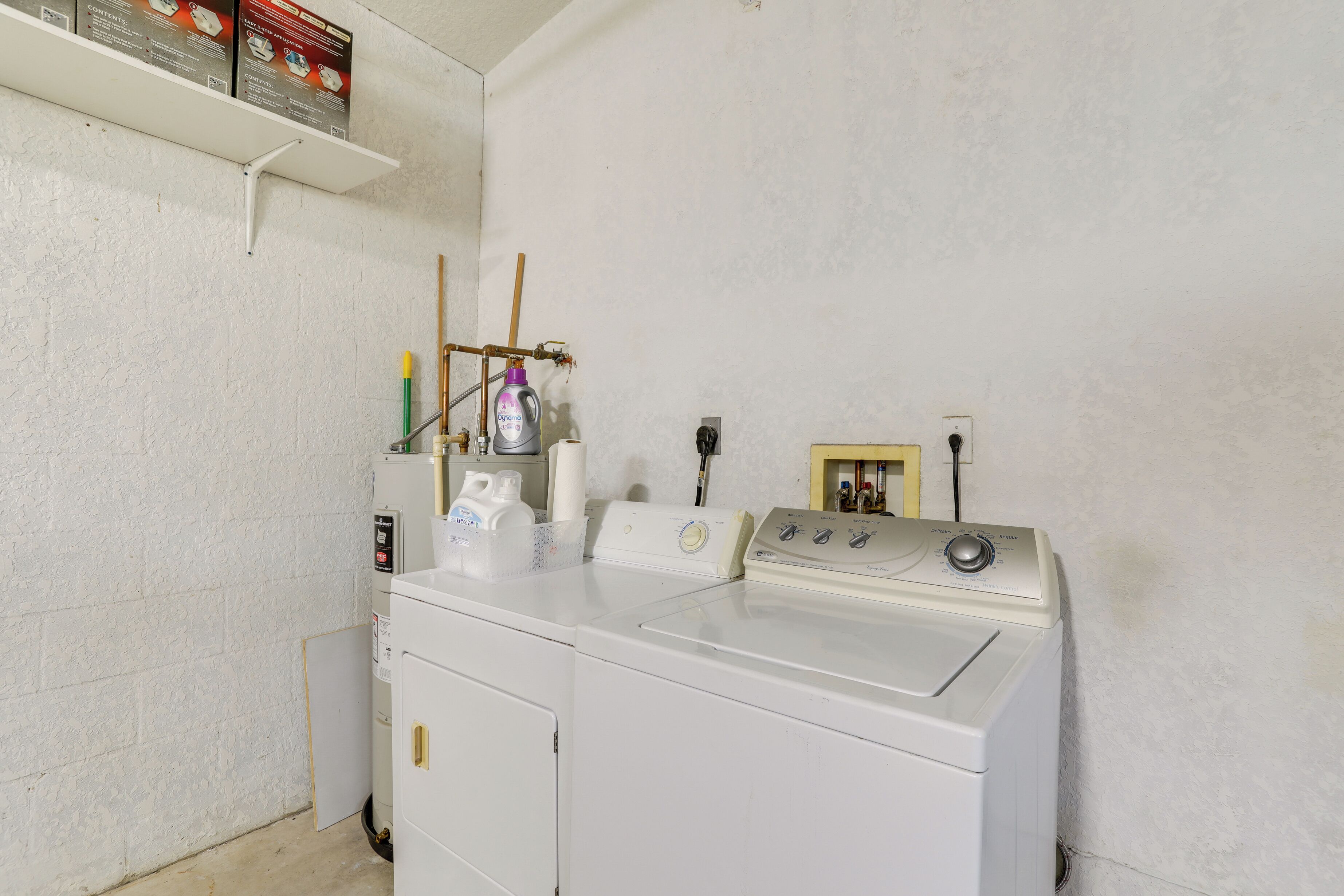 Un área de lavandería con dos lavadoras, un estante con productos de limpieza y un cuadro en la pared.