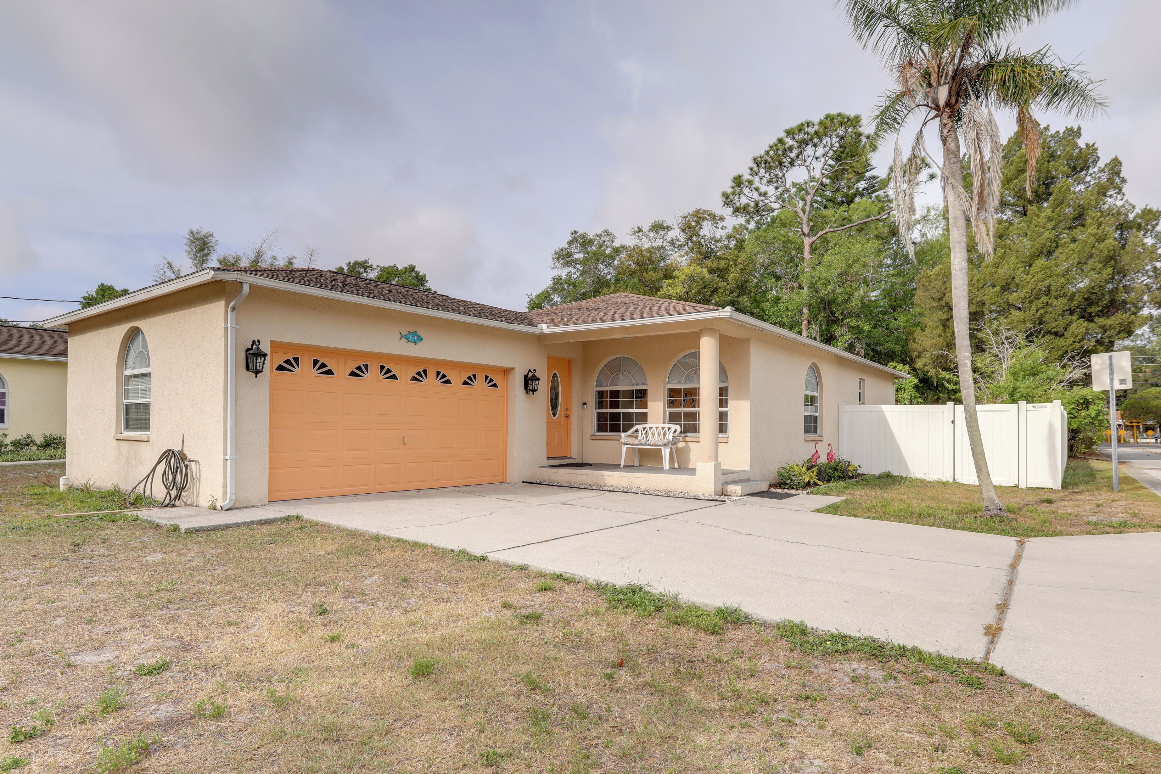 A single-story house with a garage, a front porch with a bench, and a palm tree in the background.