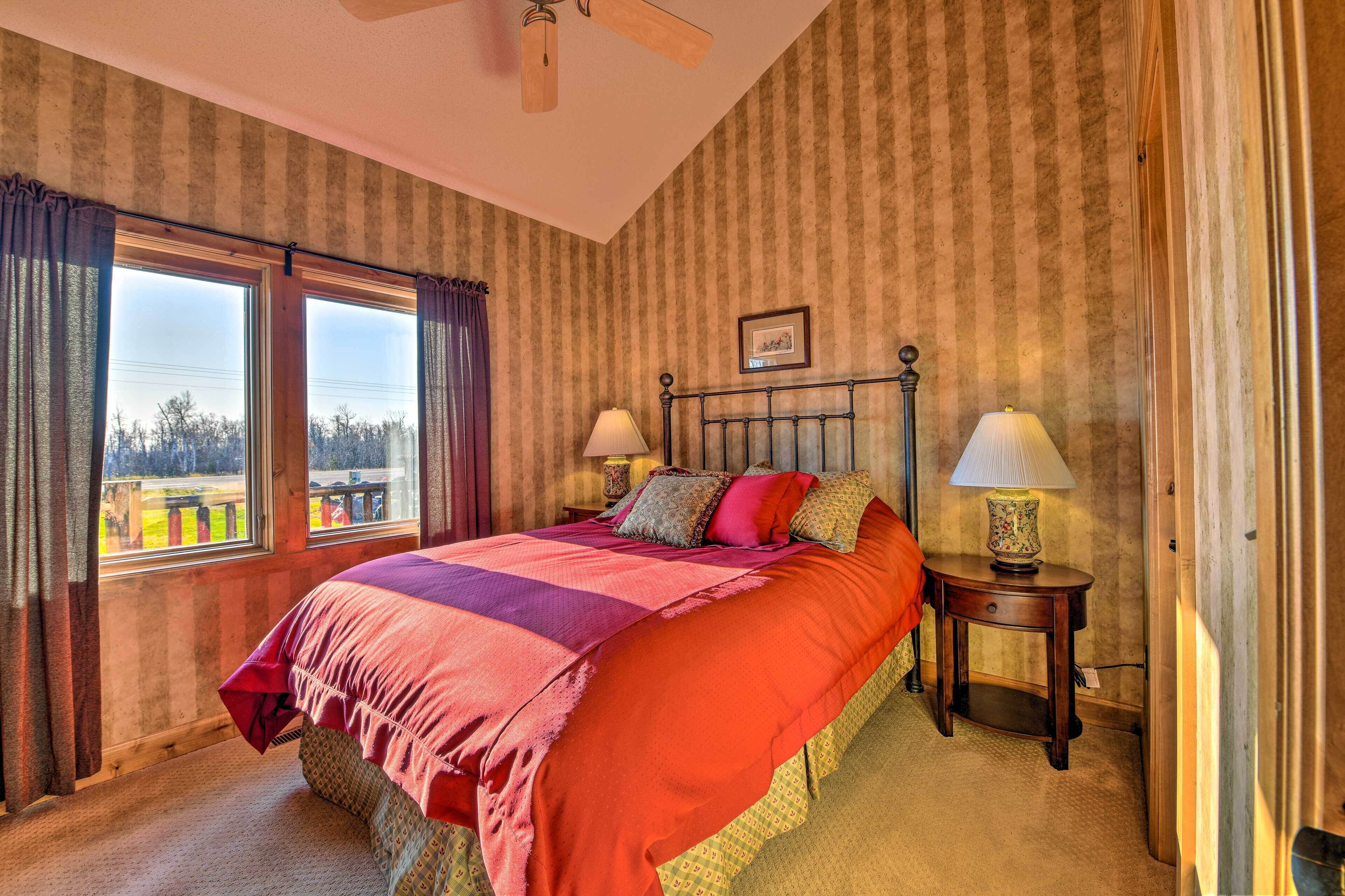 A bedroom with a large bed, two bedside tables with lamps, a ceiling fan, and a window with curtains.