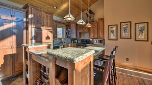 A kitchen with wooden cabinets, a granite countertop island, hanging pendant lights, and framed artwork on the wall. - North Shore Cabin w/ Fire Pit By Gooseberry Falls! (Two Harbors)