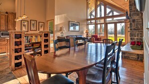 A spacious dining area with a large wooden table and chairs, surrounded by bookshelves and a stone fireplace. - North Shore Cabin w/ Fire Pit By Gooseberry Falls! (Two Harbors)