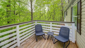A wooden deck with two wicker chairs and a small table, surrounded by a white railing, overlooking a forested area. - Camp-style Cabin Near Pigeon Forge: Fire Pit, Deck (Sevierville)