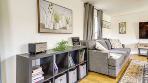 A modern living room with a grey sofa, a bookshelf, and a large painting of vases. - Camp-style Cabin Near Pigeon Forge: Fire Pit, Deck (Sevierville)