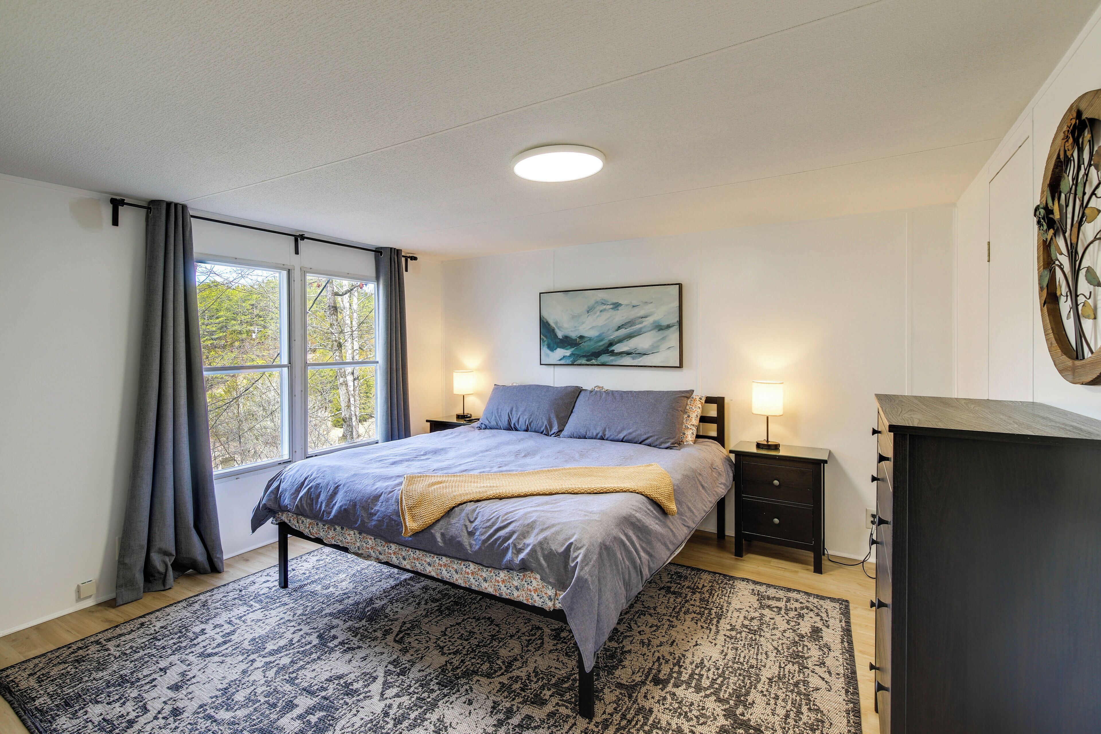 A bedroom with a bed, bedside tables, a dresser, a window with curtains, a painting on the wall, and a rug.