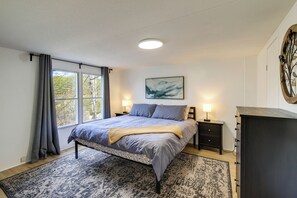 Quarto com cama, mesas de cabeceira, cômoda, janela com cortinas, um quadro na parede e um tapete.