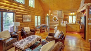 A log cabin interior with a dining area, living room with leather furniture, and a kitchen.