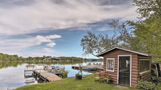 A cabin with a dock extending into a calm lake, surrounded by greenery and trees.