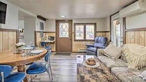 A cozy room with a wooden dining table, blue chairs, a sofa, and a television on the wall.