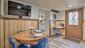 A dining area with a round wooden table, blue chairs, and a flat-screen TV mounted on the wall.