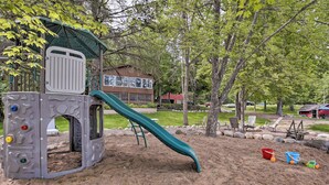 A playground with a slide and climbing structure, surrounded by trees and a building in the background.