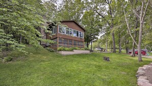 A two-story building with large windows and a stone base, surrounded by a grassy area and trees.