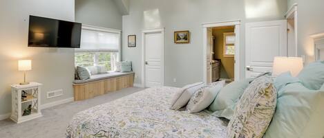 Quarto com uma cama grande, um ventilador de teto, uma TV fixada na parede e uma janela com vista.