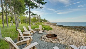 A beachside seating area with Adirondack chairs, a fire pit, and a view of the ocean. - Oceanfront Prospect Harbor House w/ Deck, View (Prospect Harbor)