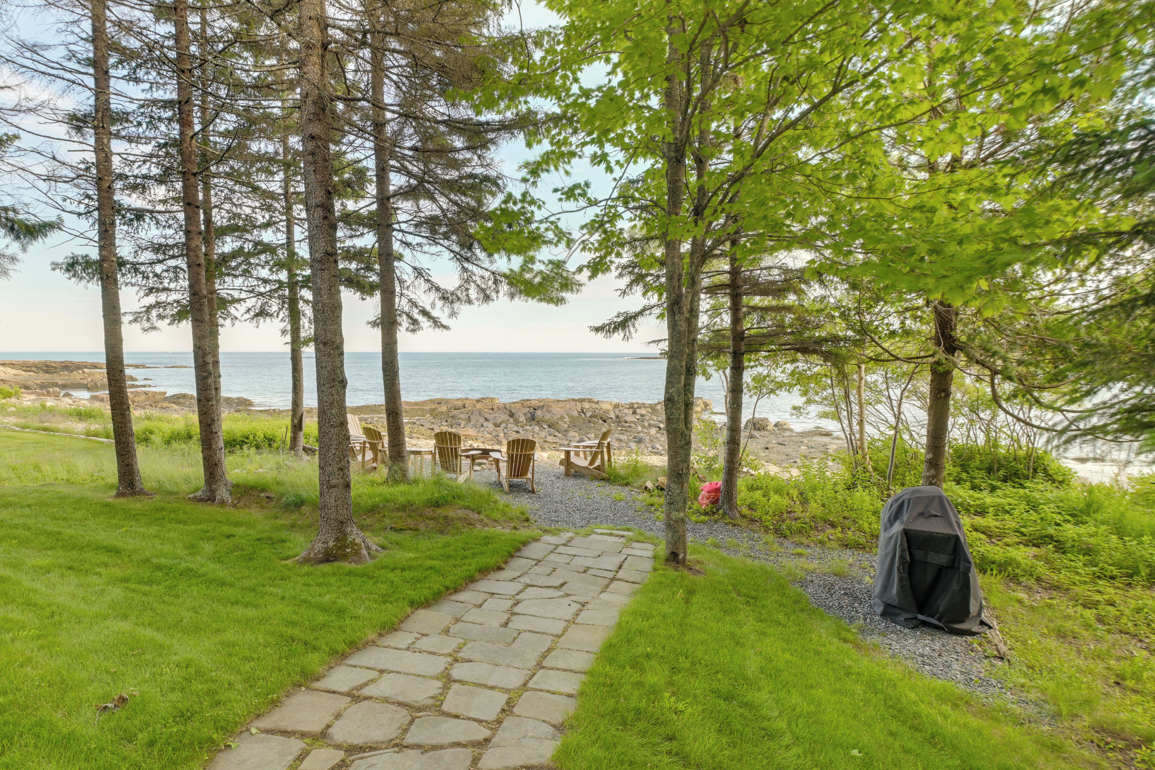 A stone pathway leading to a beach area with chairs and a tent.