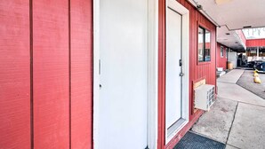 A red building with a white door and a small window. There is a concrete sidewalk and a parked car in the background. - Loveland Vacation Rental - 1 Mile to Lake! (Loveland)