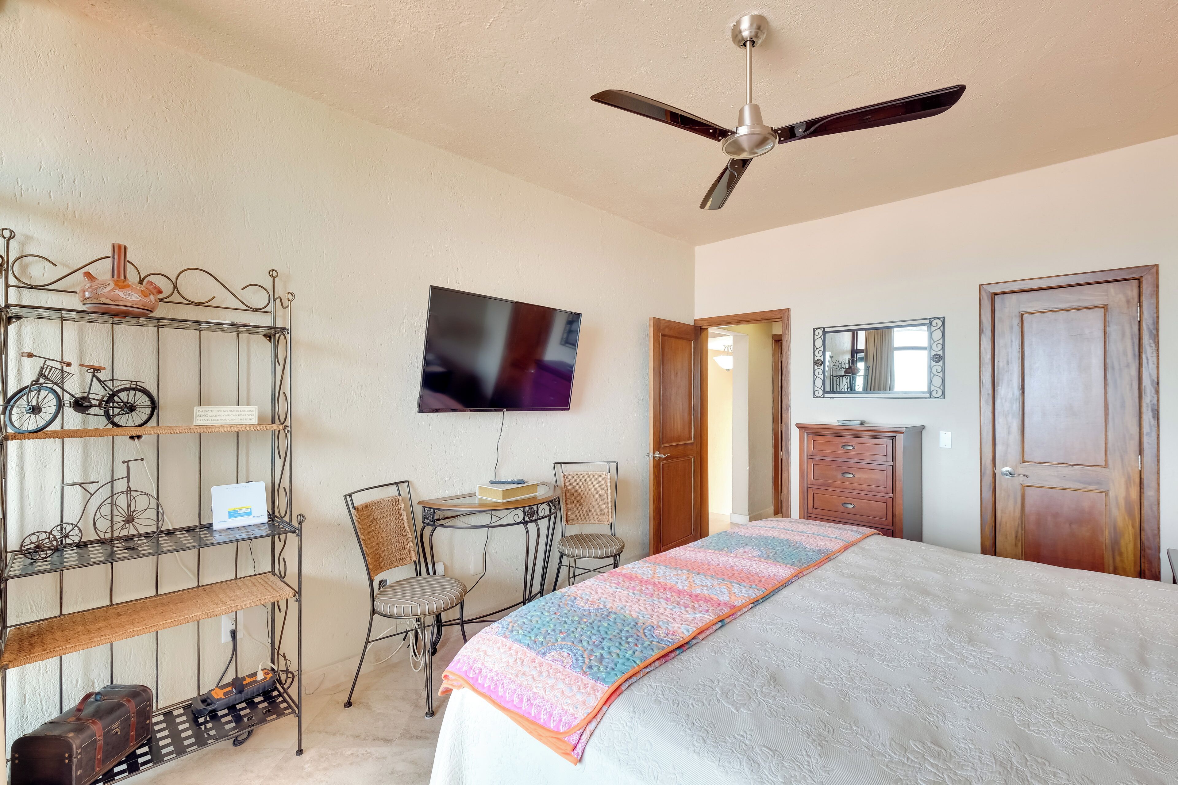 A bedroom with a bed, a desk, a chair, a TV, a wardrobe, and a mirror.