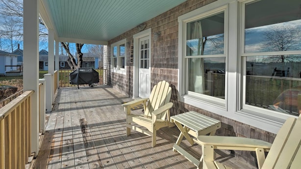 Eine überdachte Veranda mit Holzboden, Adirondack-Stühlen und einem Grill.