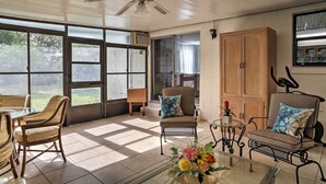 A sunlit room with a ceiling fan, large windows, wicker chairs, a glass coffee table with a floral arrangement, and a wooden cabinet. - Spacious Central Florida Home: Family Friendly! (Longwood)