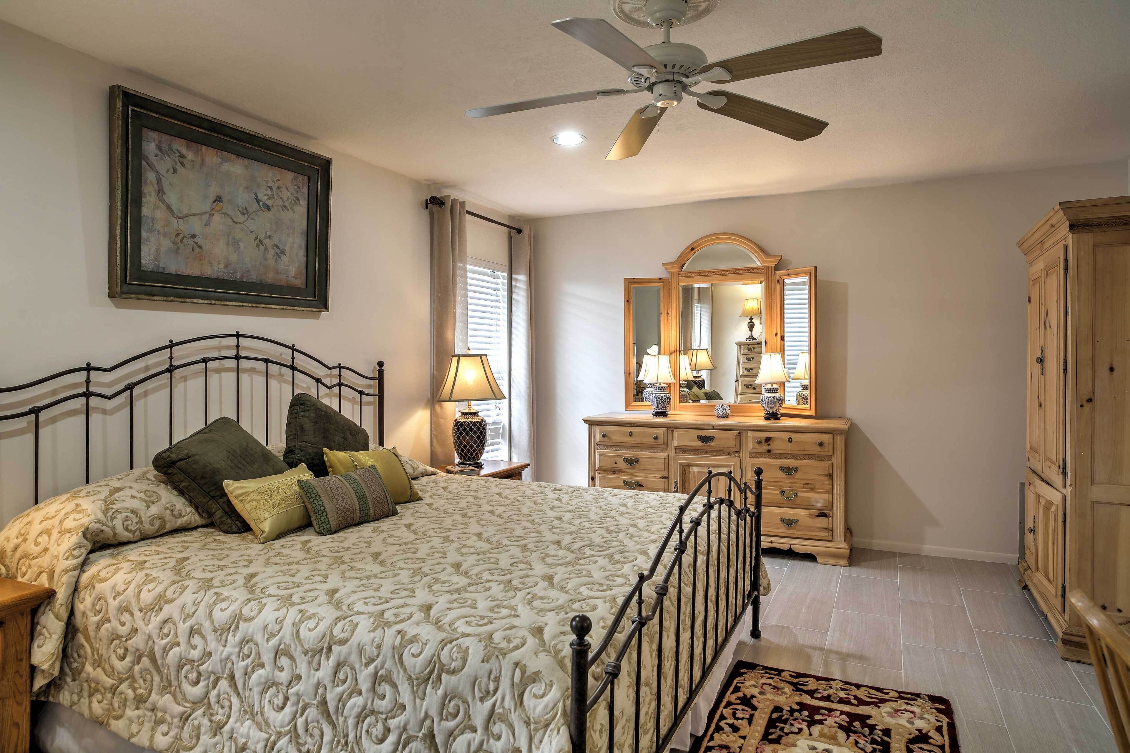 Une chambre à coucher avec un lit, un ventilateur de plafond, une commode, un miroir et un tableau accroché au mur.