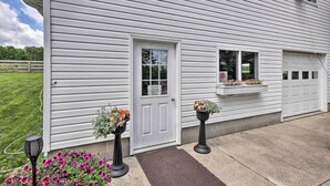 A white house with a front door, two windows, and a garage door. There are flower planters in front of the house. - Loft Unplugged w/ Outdoor Space in Amish Country! (Middlefield)