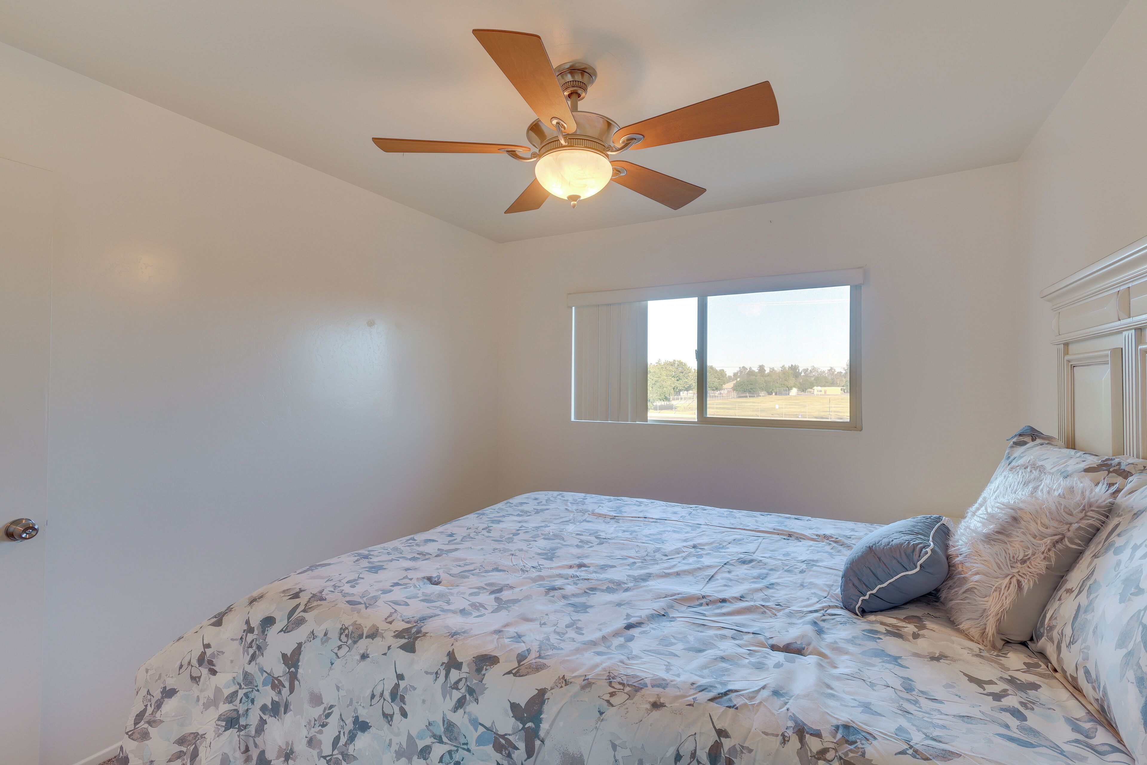 A bedroom with a bed, a ceiling fan, a window, and a view of the outdoors.