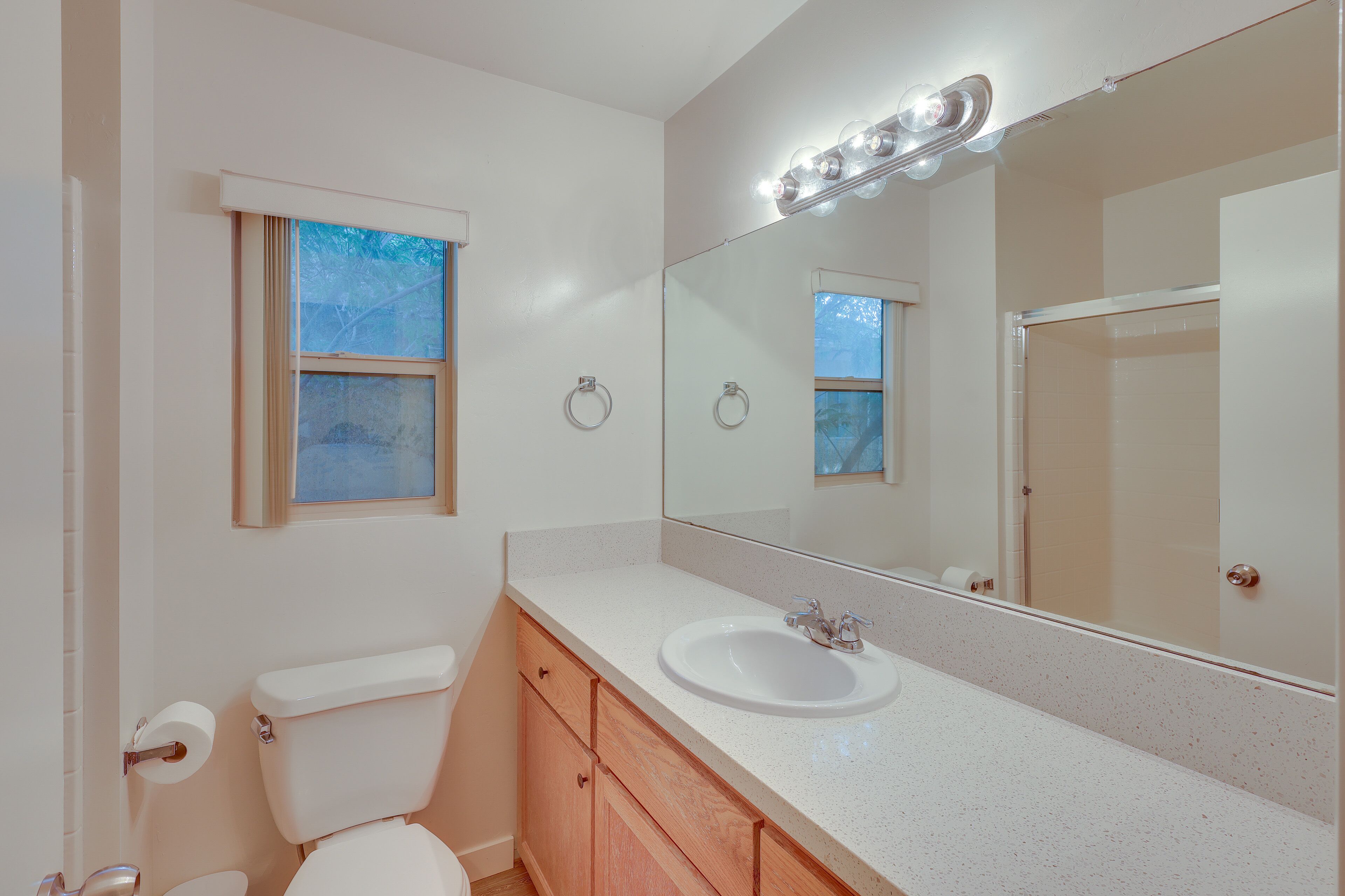 A bathroom with a white toilet, a sink, a mirror with lights, and a window.