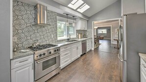Une cuisine moderne équipée d’une cuisinière à gaz, d’un four et d’un lave-vaisselle, avec des meubles blancs, un dosseret décoratif, des fenêtres de toit et une vue sur la salle à manger.