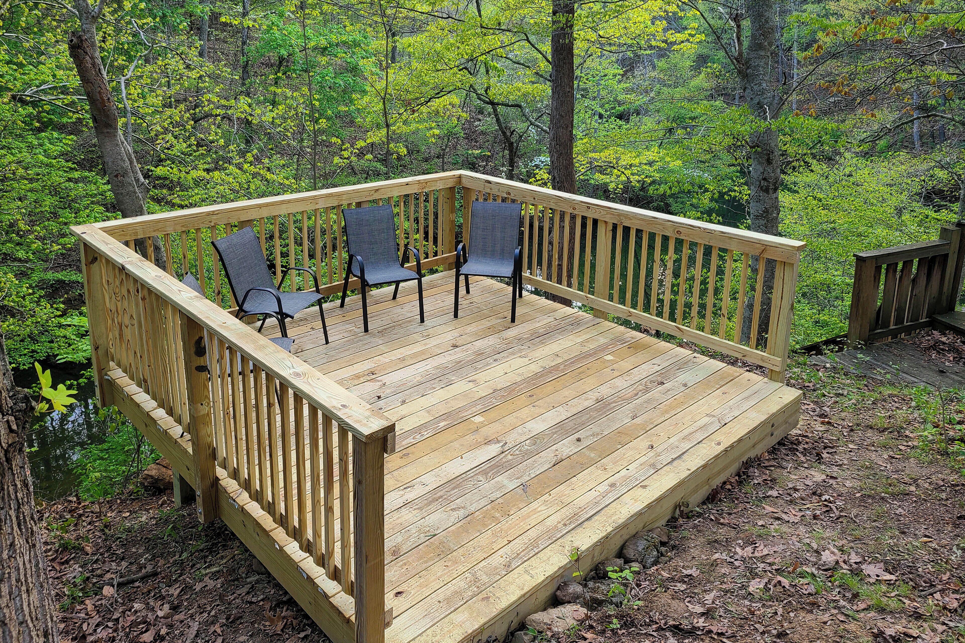 Una terraza de madera con sillas, rodeada por un bosque.