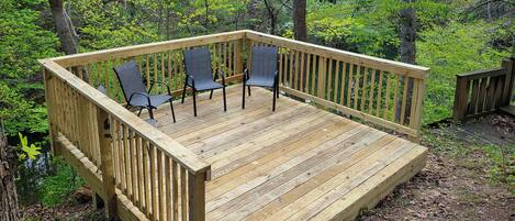 Una terraza de madera con sillas, rodeada por un bosque.