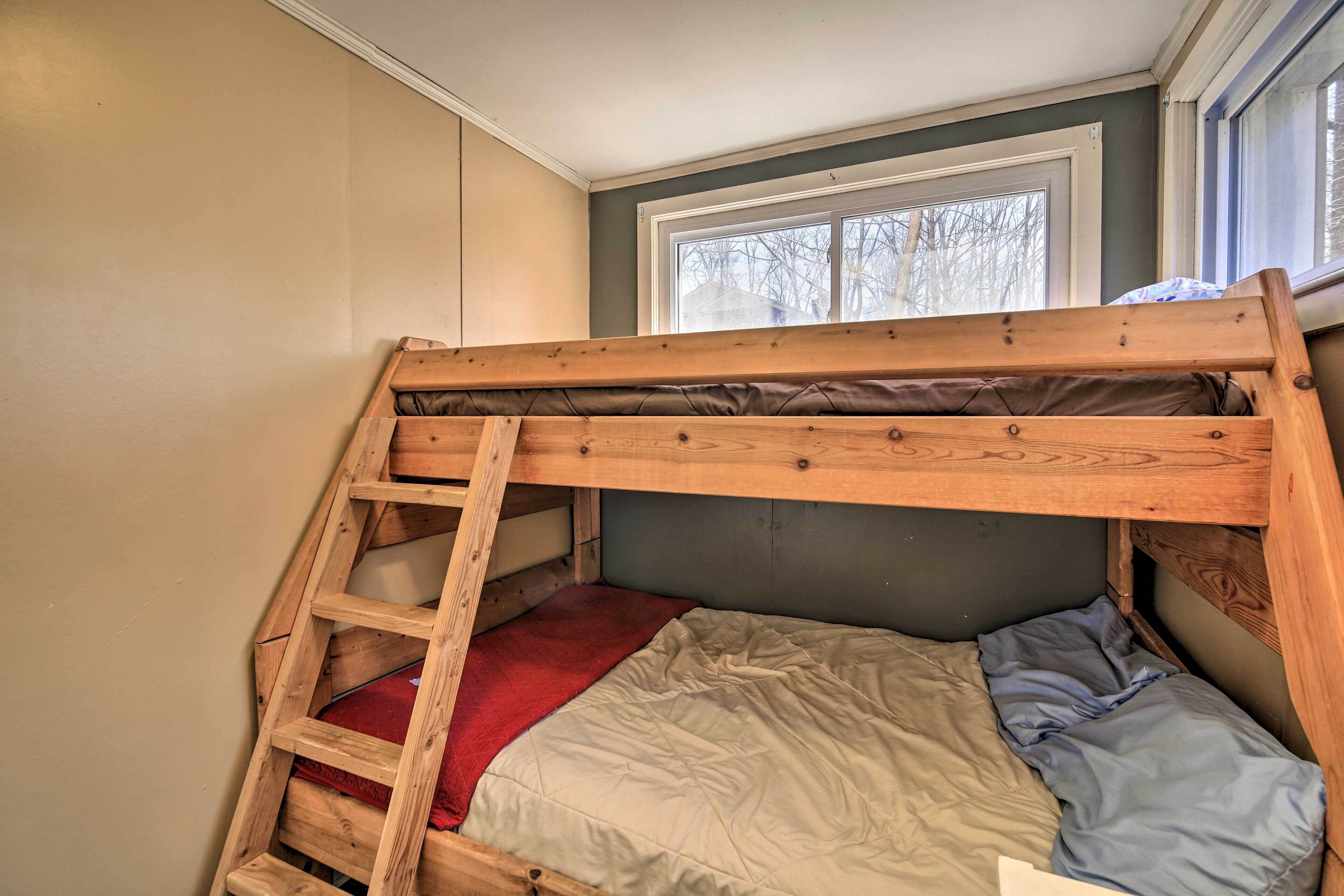 Ein Stockbett mit Holzleiter, einer roten Decke und einem blauen Kopfkissen.