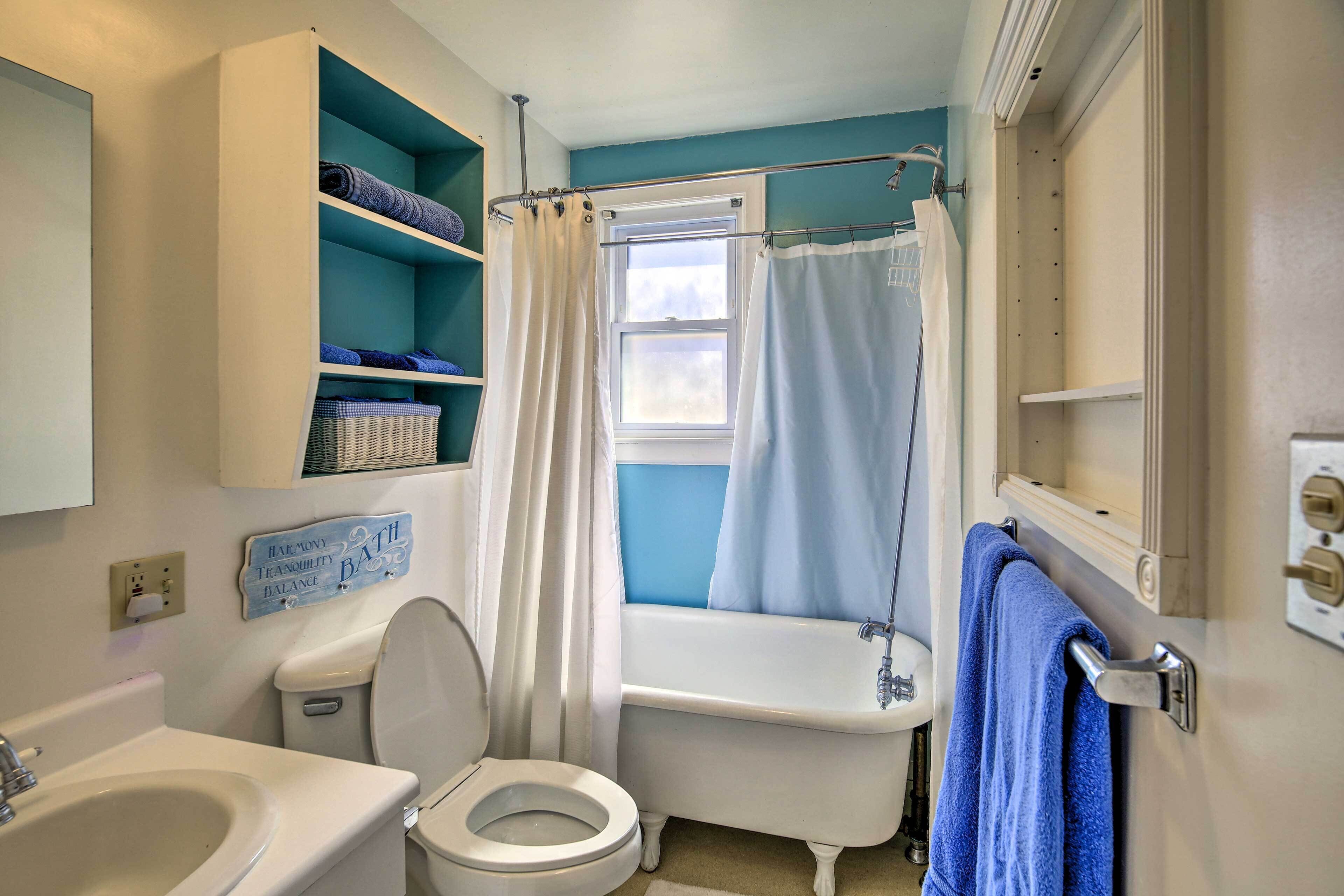 Een badkamer met toilet, wastafel, bad en een raam met douchegordijn.