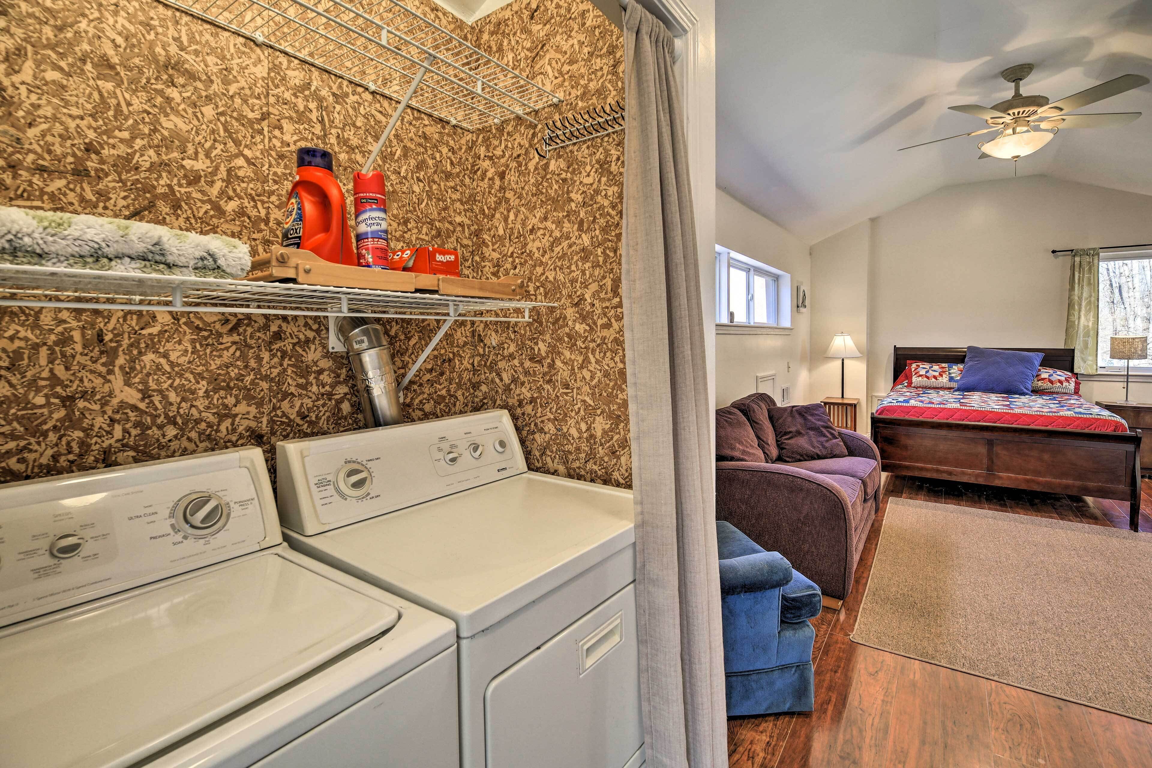 A laundry area with two washing machines, a drying rack, and shelves with cleaning supplies.