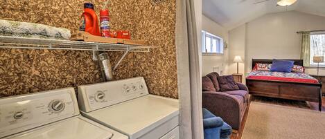 A laundry area with two washing machines, a drying rack, and shelves with cleaning supplies.