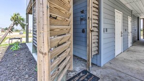 A wooden gate leading to a house with a blue door, a concrete porch, and a small garden area with mulch and a palm tree. - Mexico Beach Getaway w/ Balcony & Ocean Views! (Port St. Joe)