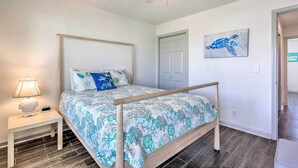 A bedroom with a bed, nightstand, lamp, ceiling fan, and a door. - Mexico Beach Getaway w/ Balcony & Ocean Views! (Port St. Joe)