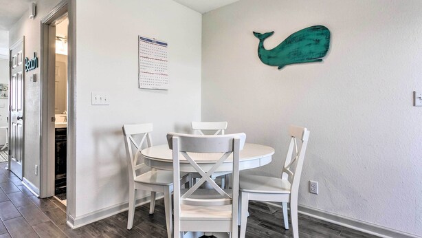 A dining area with a round table and four white chairs, a calendar on the wall, and a teal whale decoration. - Mexico Beach Getaway w/ Balcony & Ocean Views! (Port St. Joe)