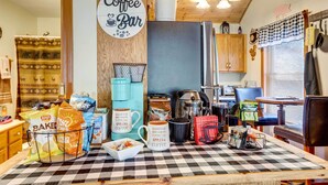 Un coin cuisine avec un panneau indiquant un bar à café, divers appareils de cuisine et une nappe à carreaux.