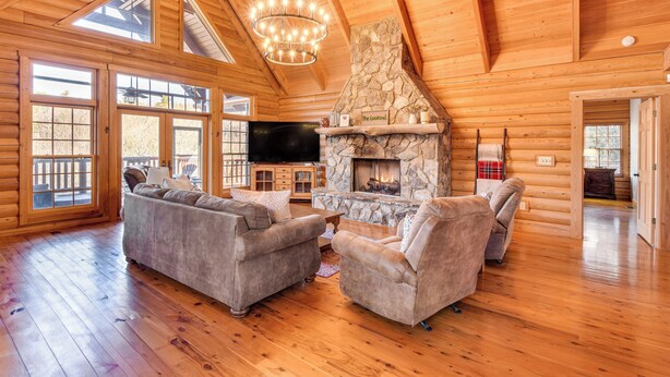 Un intérieur spacieux de chalet en bois avec une cheminée en pierre, des planchers en bois et un grand téléviseur.