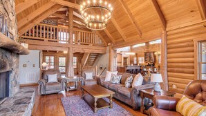 Un intérieur spacieux de chalet en bois, avec une cheminée en pierre, des meubles en cuir et un grand lustre.