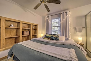 A bedroom with a bed, wooden shelving unit, window with curtains, and a ceiling fan.