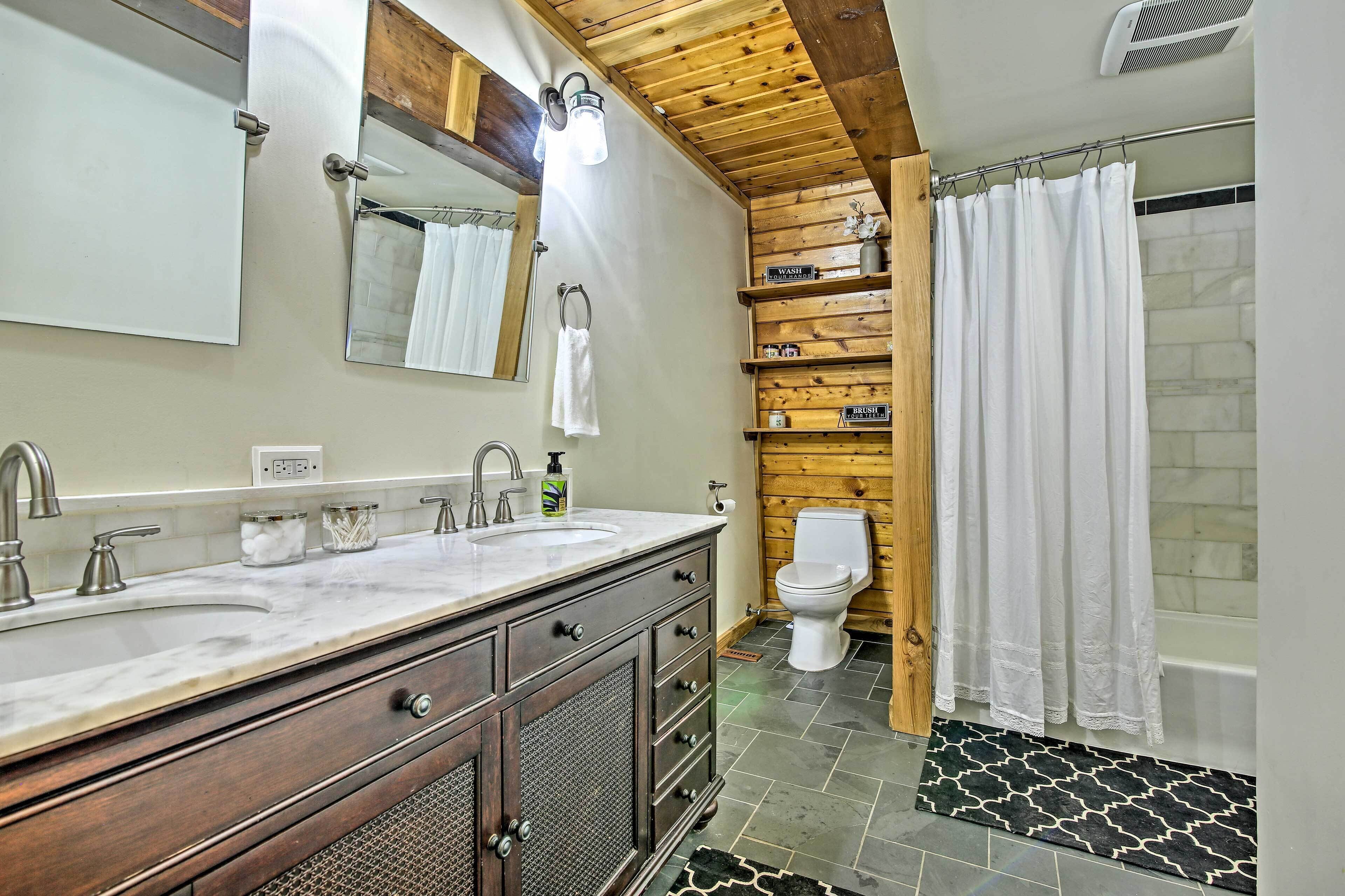 A bathroom with a wooden vanity, a double sink, a toilet, and a shower curtain.