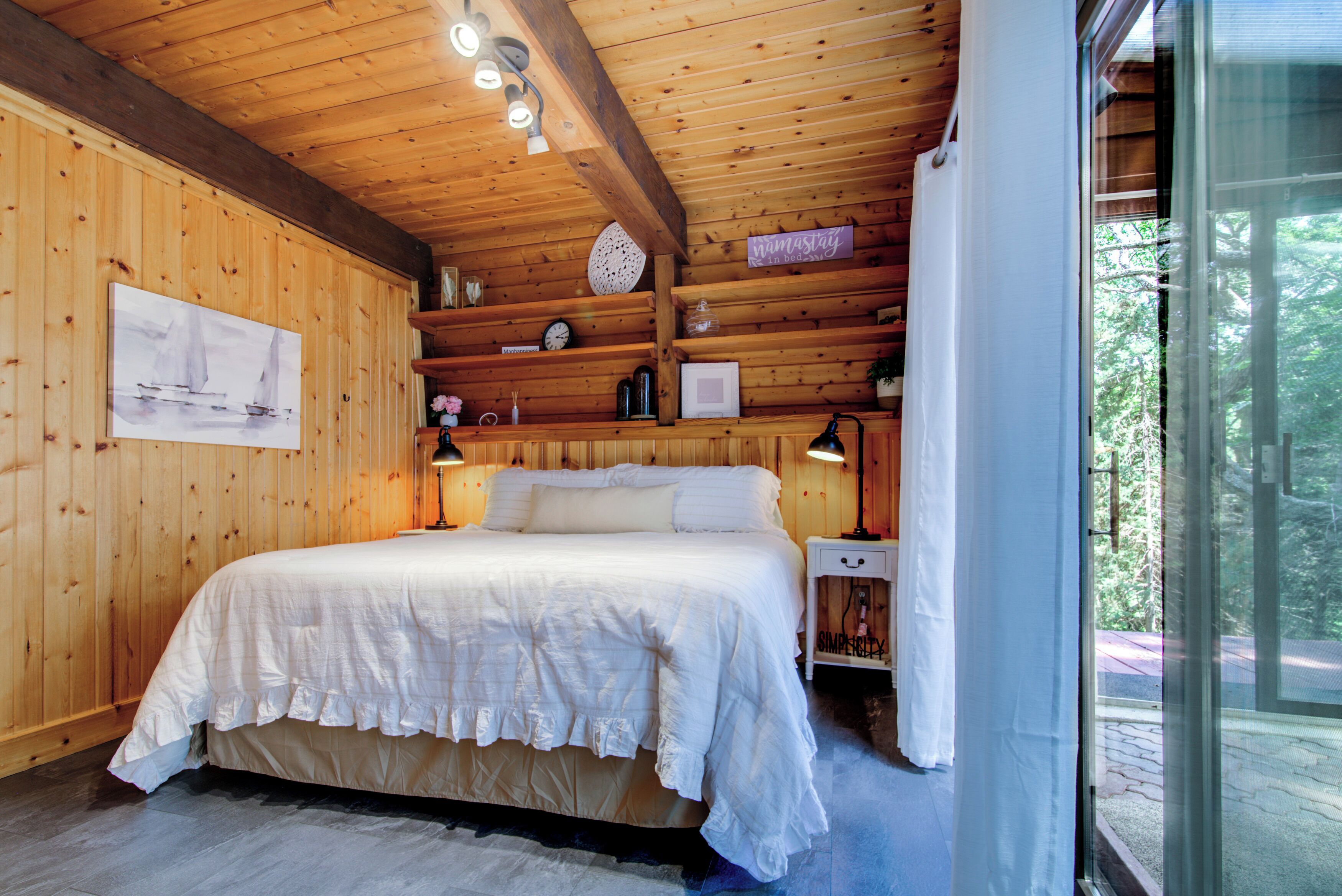 A wooden cabin bedroom with a large bed, bedside tables, and a window with a view of the outdoors.