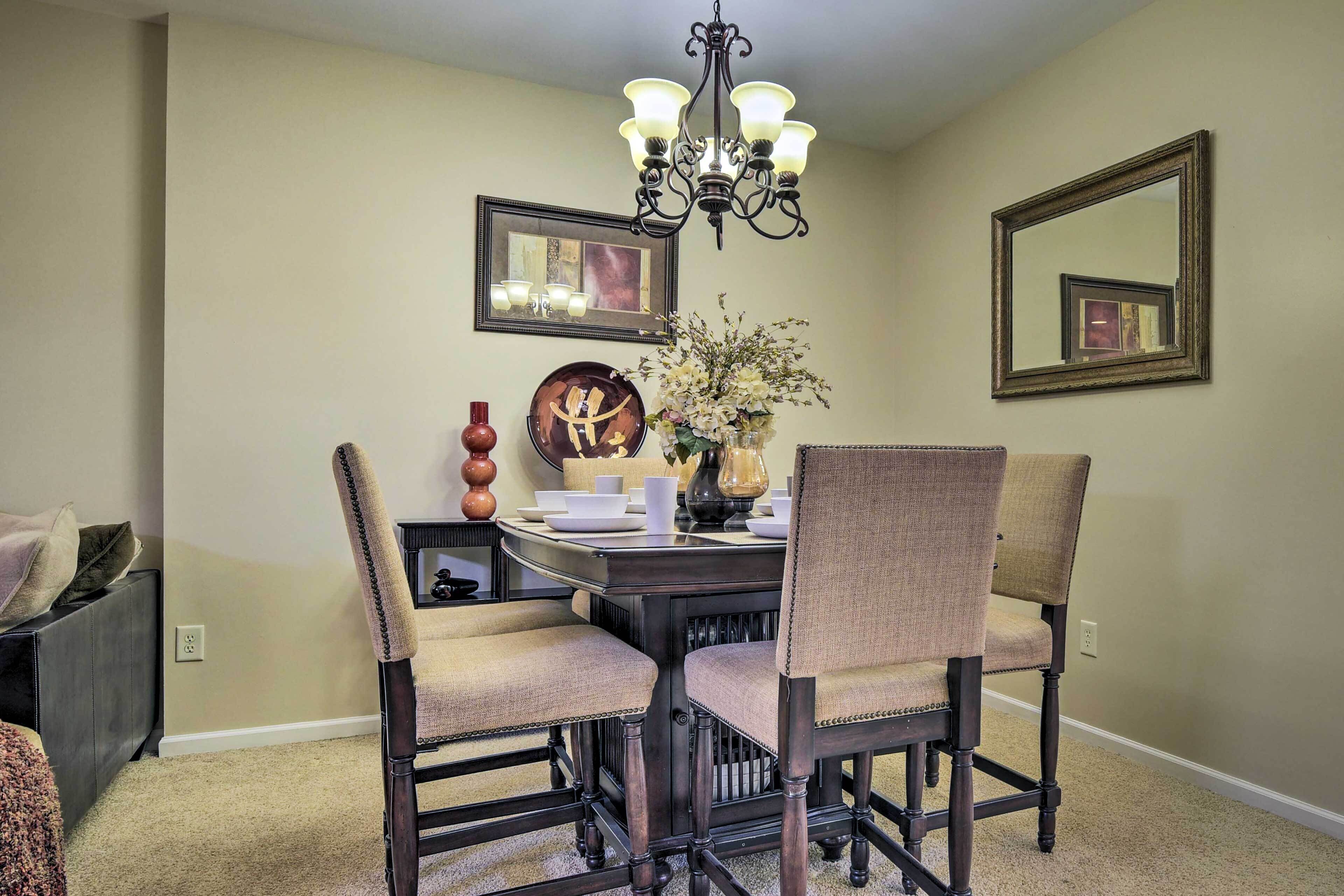 A dining area with a dark wooden table, beige upholstered chairs, a chandelier, and wall-mounted artwork.